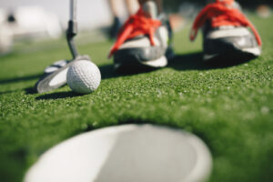 Kids play mini golf. Close-up image of player in sneakers with mini golf club and white golf ball.